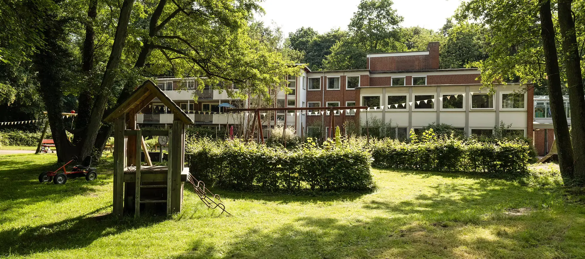 Grüne Spielwiese mit Kletterhaus und Schaukeln vor einem Backsteinhaus mit mehreren Balkonen