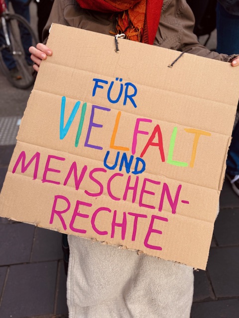 Ein Pappschild mit der Aufschrift: "Für Vielfalt und Menschenrechte" in bunten Farben.